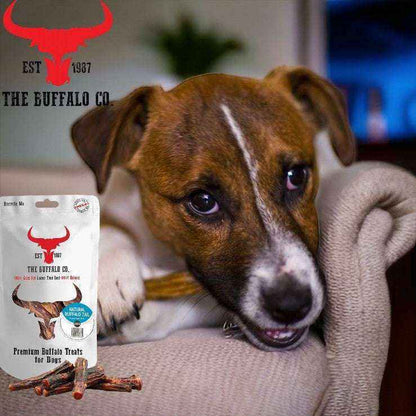 Buffalo Tail - Dog Treats in a natural brown chew, shown beside recyclable packaging with a dog enjoying a chew